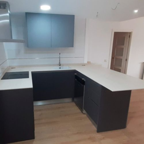 Muebles de cocina en madera oscura, encimera blanca y mueble alto en gris