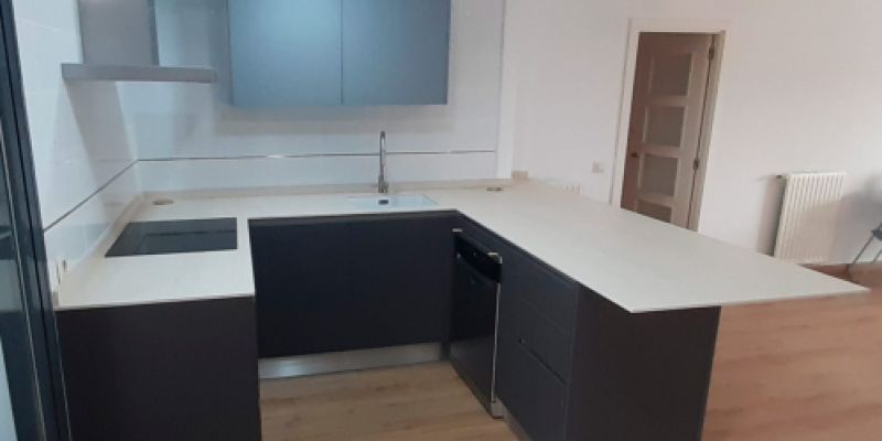 Muebles de cocina en madera oscura, encimera blanca y mueble alto en gris