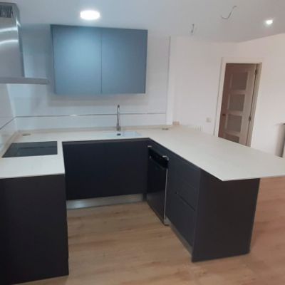 Muebles de cocina en madera oscura, encimera blanca y mueble alto en gris